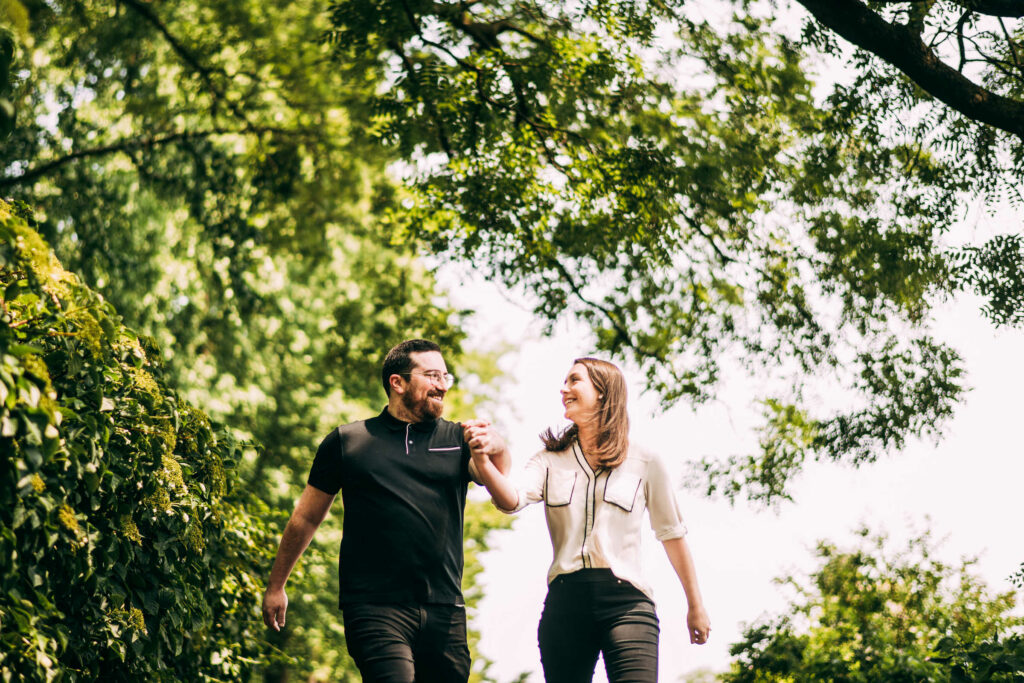A couple holds hands and runs downhill under tree cover during their Brooklyn Botanic Garden engagement session.