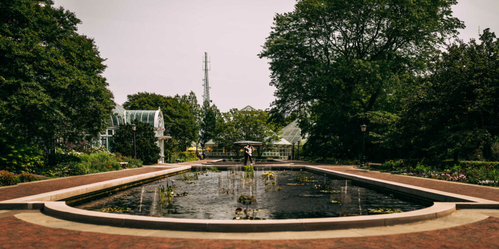 A couple stands at the far end of a living pond in a courtyard during their Brooklyn Botanic Garden engagement session.