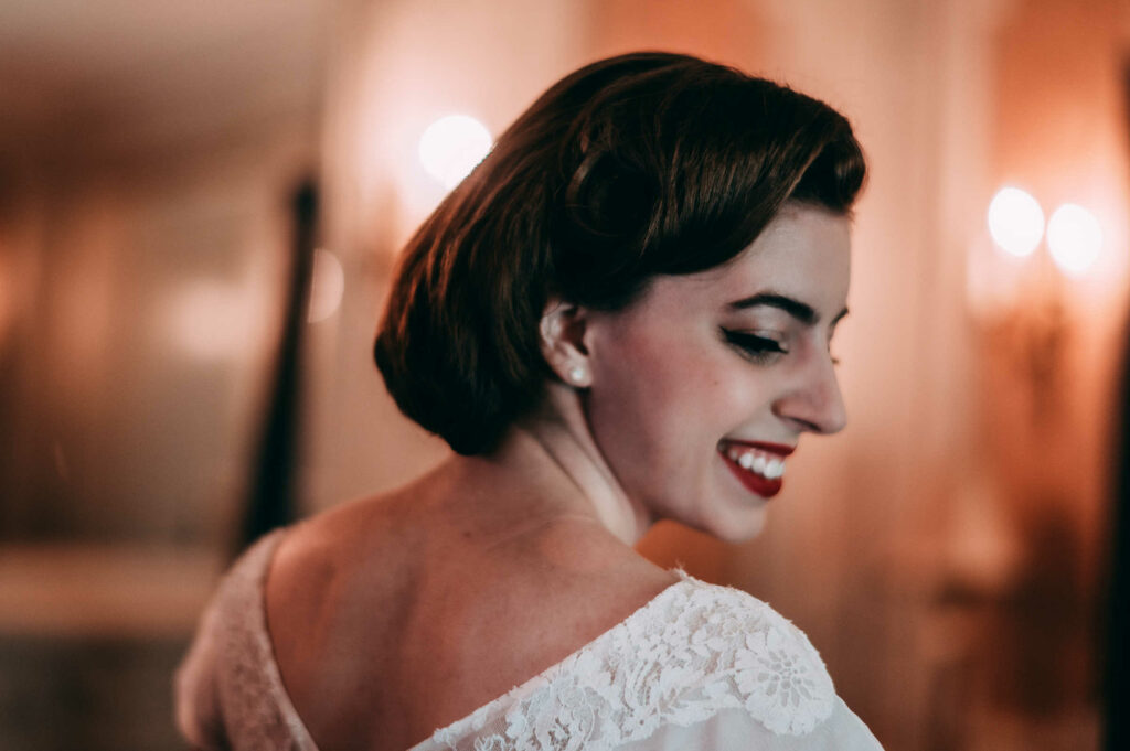 A bride looks over her right shoulder and smiles before her intimate New Hampshire wedding at the Silver Fountain Inn.