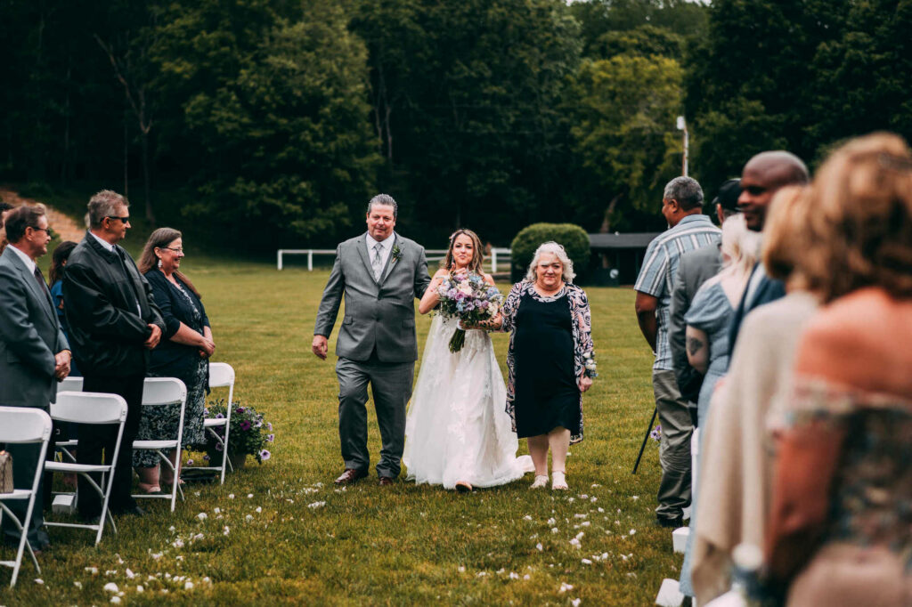 A bride is walked down the aisle by her parents during her campground wedding.