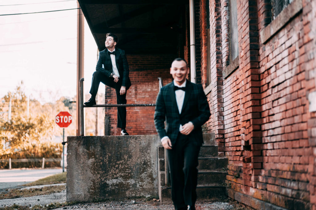 Two grooms pose in an industrial setting outside during their wedding at BAD SONS Beer Company.