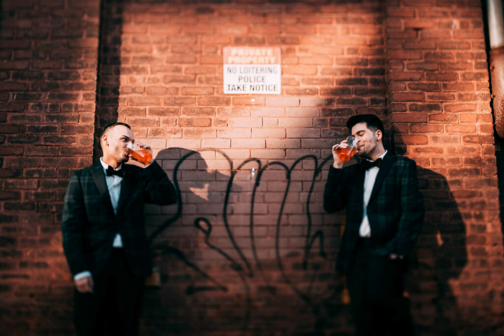 Two grooms enjoy sips of beer during their wedding at BADSONS beer company.