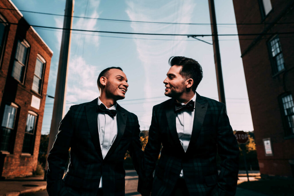 Two grooms smile and walk together at brewery CT wedding venue BADSONS.