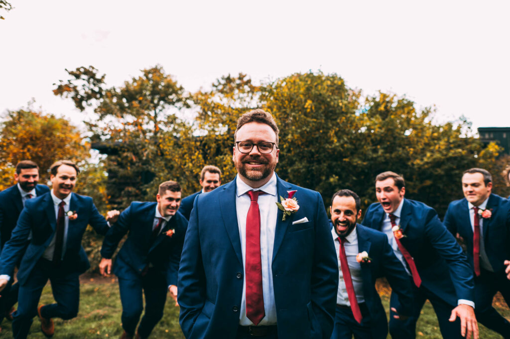 A groom with his hands in his pants pockets gets rushed from behind by his groomsmen during his wedding at Castle Hill Inn.