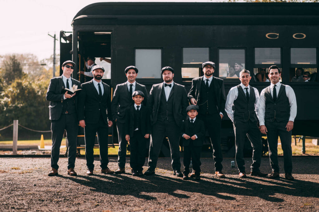 A groom and his groomsmen stand in front of the Essex Steam Train before his wedding at The Lace Factory.