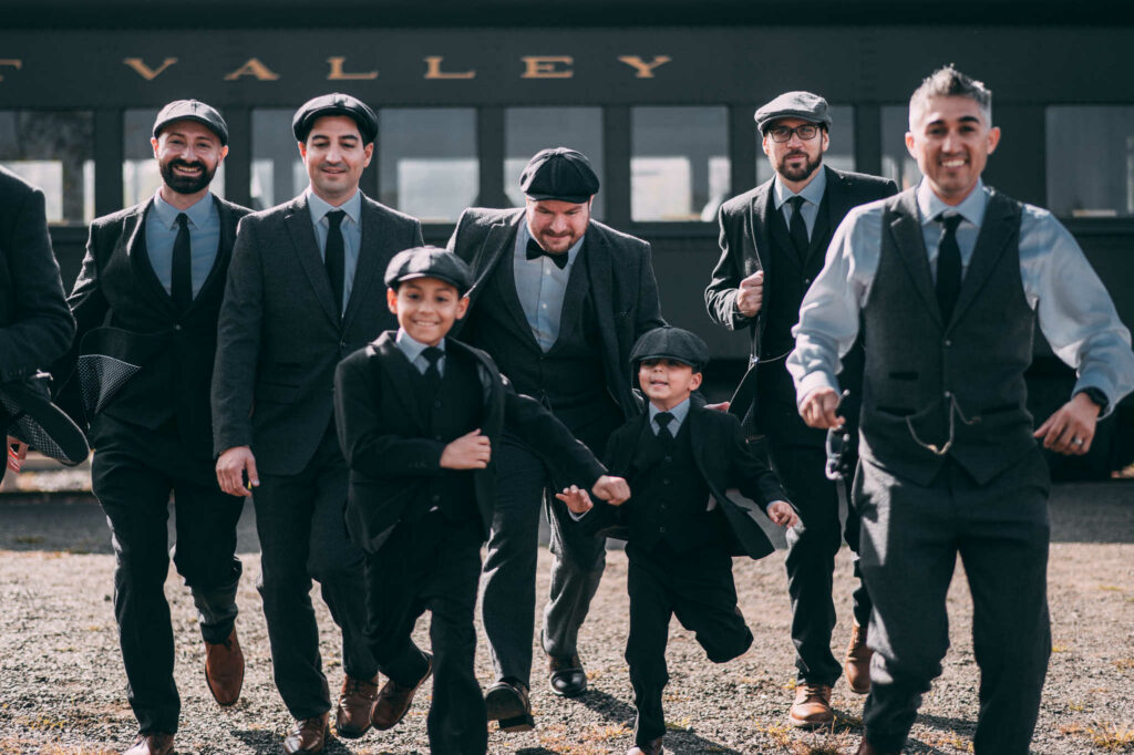 A groom and his groomsmen are dressed like Peaky Blinders characters for his Lace Factory wedding with a steam train behind them.