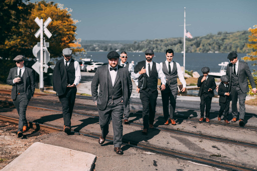 A group of groomsmen walk with the groom over train tracks at Deep River Landing, CT on the way to his Lace Factory wedding.