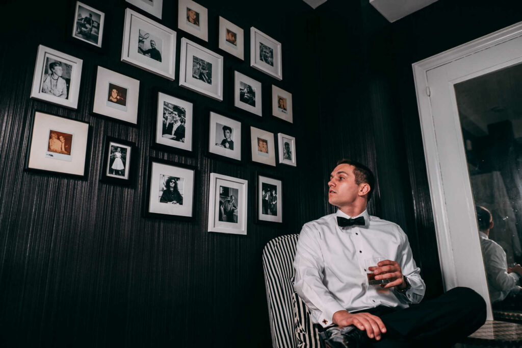 A groom takes a break in a chair with a glass of bourbon while getting ready for his Graduate Providence wedding day.