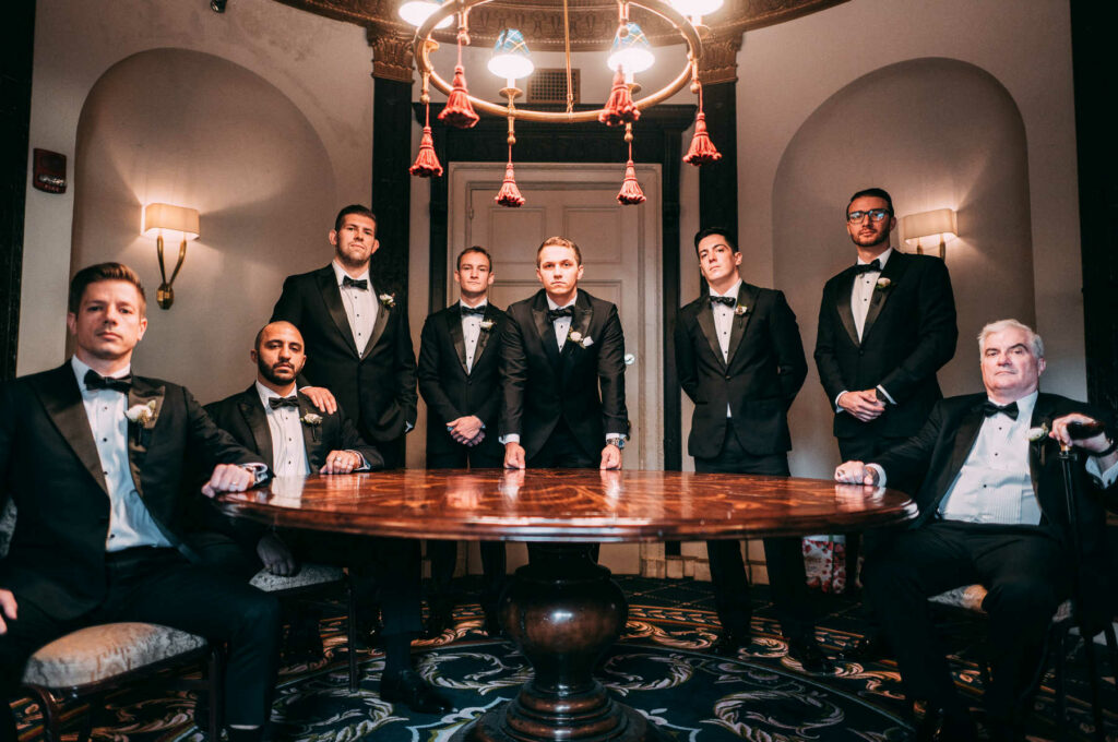 The groom and his groomsmen pose together with serious faces around a large wooden table during his Graduate Providence wedding day.