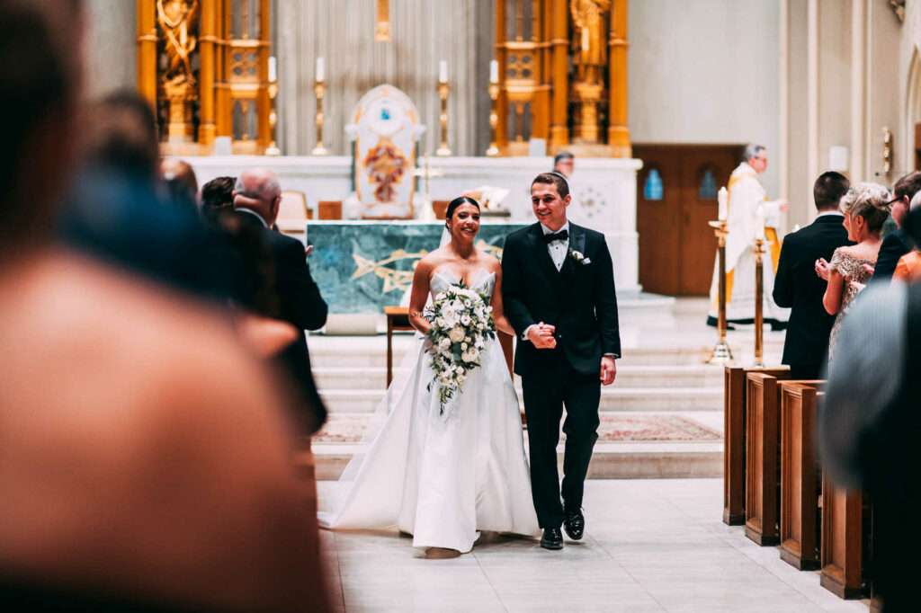 The bride and groom walk arm in arm out of the church on their way to their Providence Biltmore wedding reception.