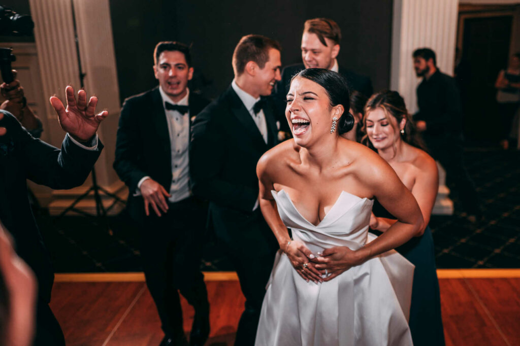 A bride in a white wedding dress laughs with her guests on the dance floor of her wedding at Graduate Providence.