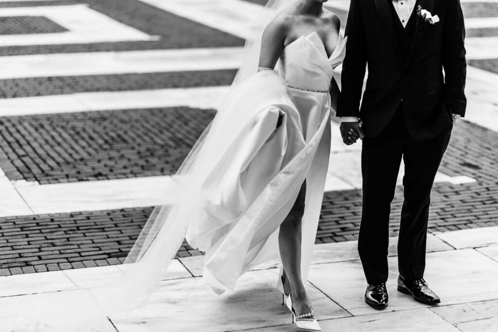A bride holds the train of her dress while holding hands with her groom on their wedding day at the Rhode Island State house.