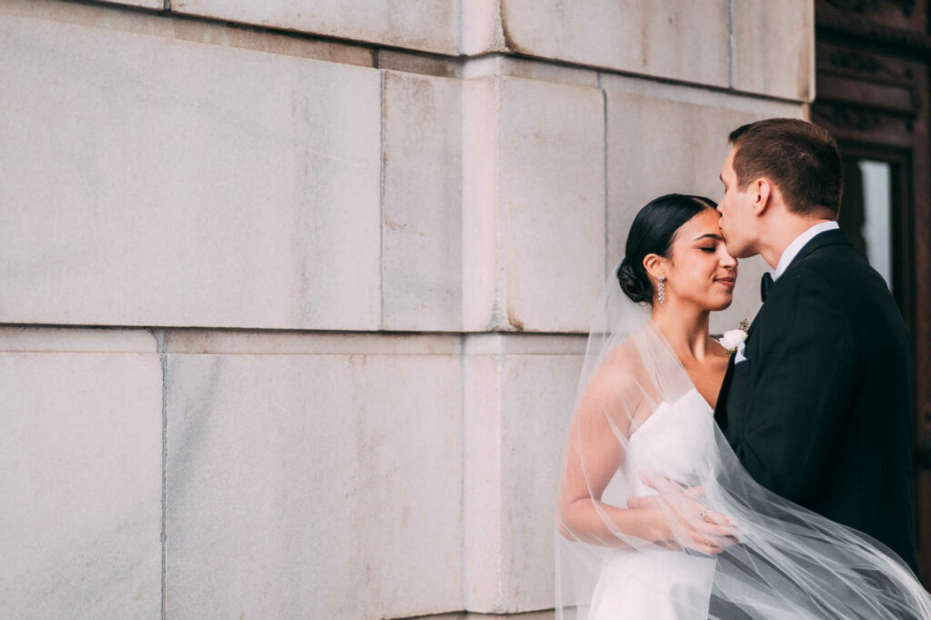 The bride and groom pose against a wall at Rhode Island State House before their Providence Biltmore wedding.